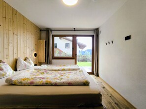 A hotel room with two beds, wooden walls, a large window, and a view of a building and greenery outside. - SiLENA Family Apartment (Lajen)