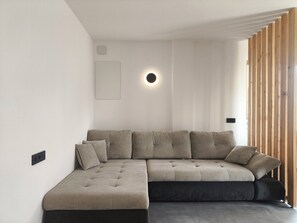A modern living room with a sectional sofa, a wall-mounted circular light, and a wooden slat partition. - SiLENA Family Apartment (Lajen)