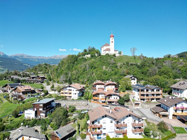 A residential area with houses on a hillside, a prominent church with a bell tower, and a clear blue sky. - SiLENA Family Apartment (Lajen)