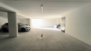 Autotalli, jossa on kaksi parkissa olevaa autoa, betonipilarit ja ovi oikealla puolella.