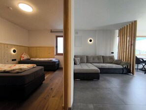 A modern living room with a sectional sofa, two single beds, wooden flooring, and built-in ceiling lights. - SiLENA Family Apartment (Lajen)