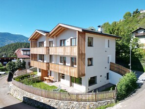 A multi-story building with balconies, a stone wall, and a view of the mountains. - SiLENA Family Apartment (Lajen)