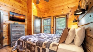 Ein Schlafzimmer in einer Holzhütte mit einem Bett, einem Schminktisch und einem Bild an der Wand.