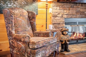 Un intérieur en bois avec une cheminée, un panneau d’accueil en forme d’ours et un fauteuil à motifs floraux.
