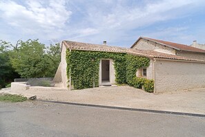 Un bâtiment avec un toit recouvert de tuiles, une porte ouverte et une allée gravillonnée.