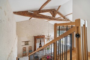 Un intérieur rustique avec des poutres apparentes, un escalier doté d’une rampe en bois et un lustre.