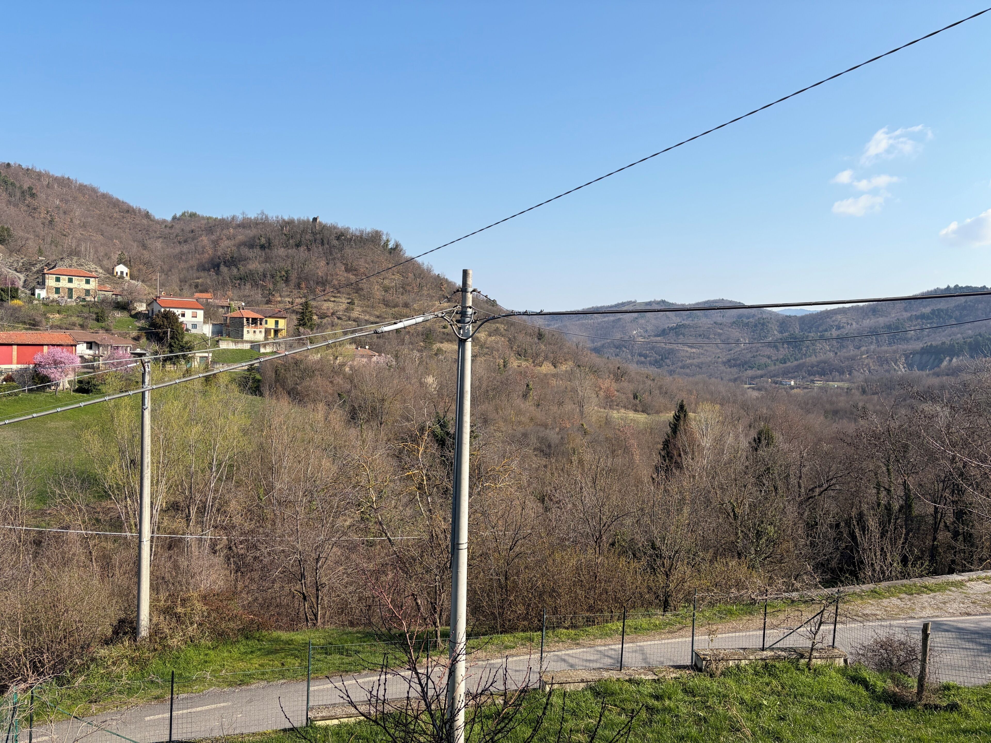 Un paysage rural avec des maisons sur une colline, une route et des lignes électriques.