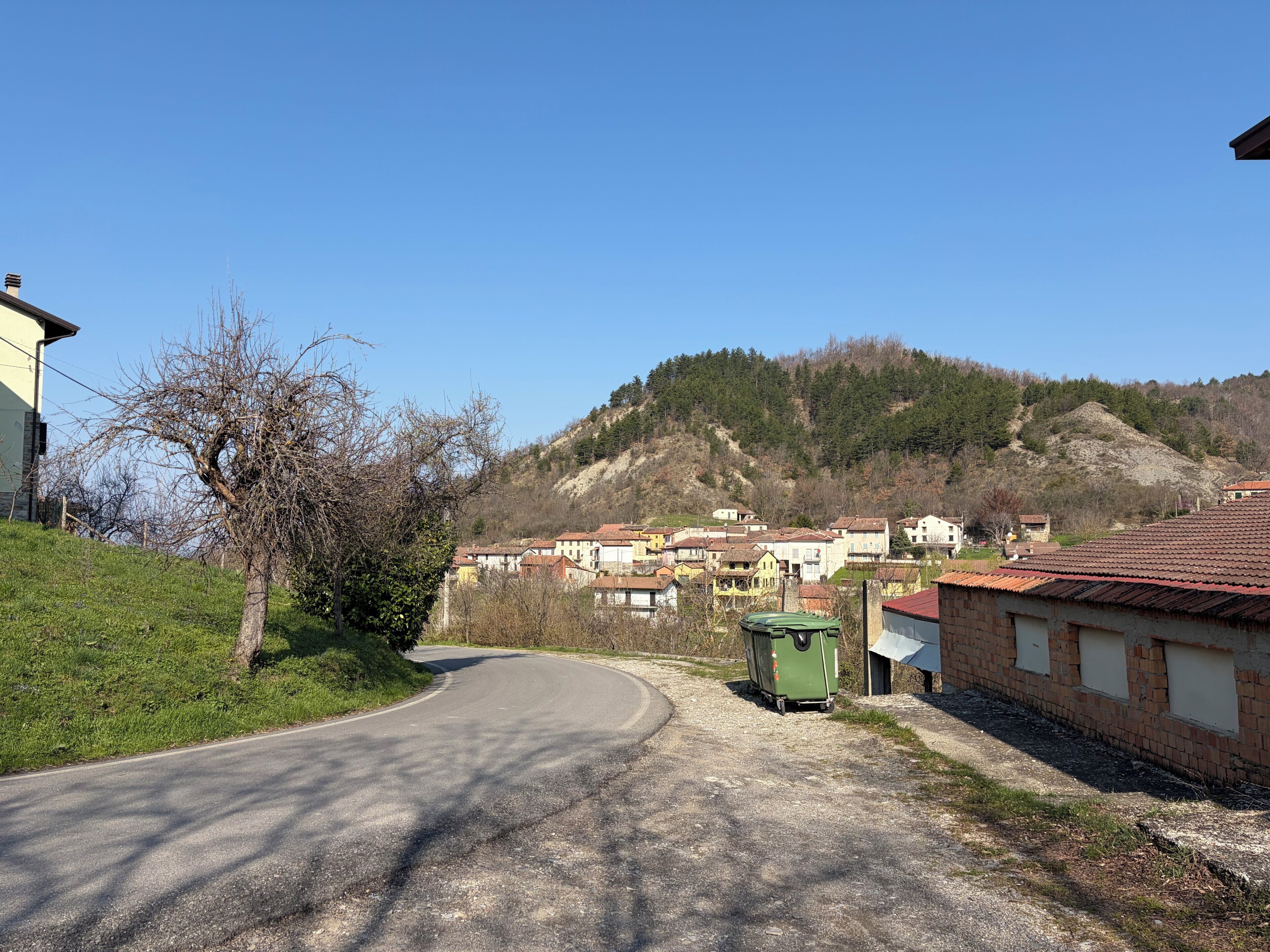 Une route de campagne sinueuse traverse un village, avec des maisons et une colline en arrière-plan.