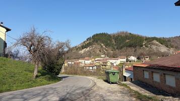 Une route de campagne sinueuse traverse un village, avec des maisons et une colline en arrière-plan.
