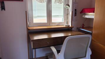 A study room with a wooden desk, a white office chair, a window with blinds, a desk lamp, and a calendar on the wall.