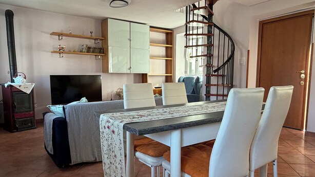 Un espace repas comprenant une table, des chaises, un téléviseur, une bibliothèque et un escalier en colimaçon.