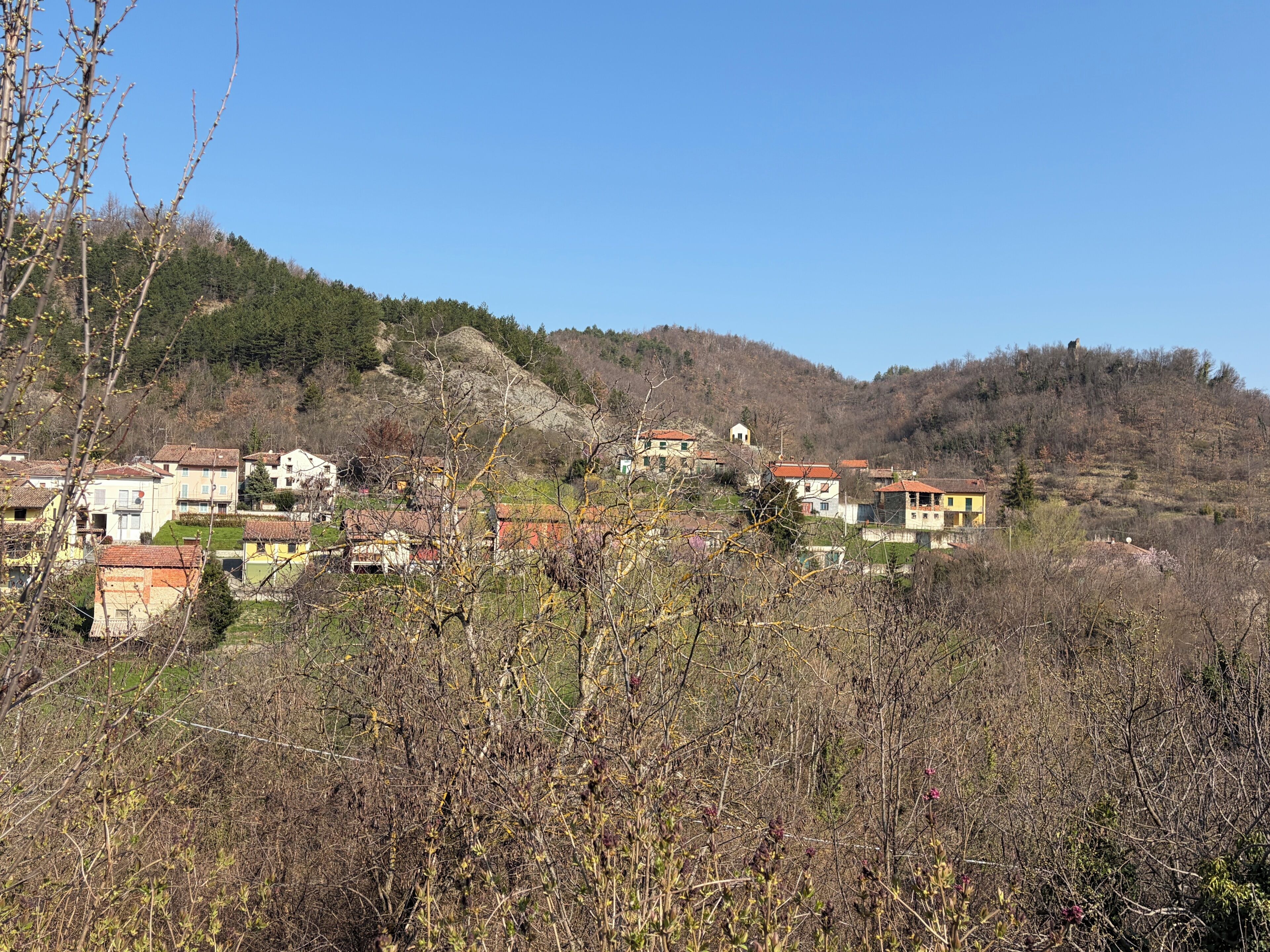 A hillside village with traditional buildings, some with red roofs, and a clear blue sky.