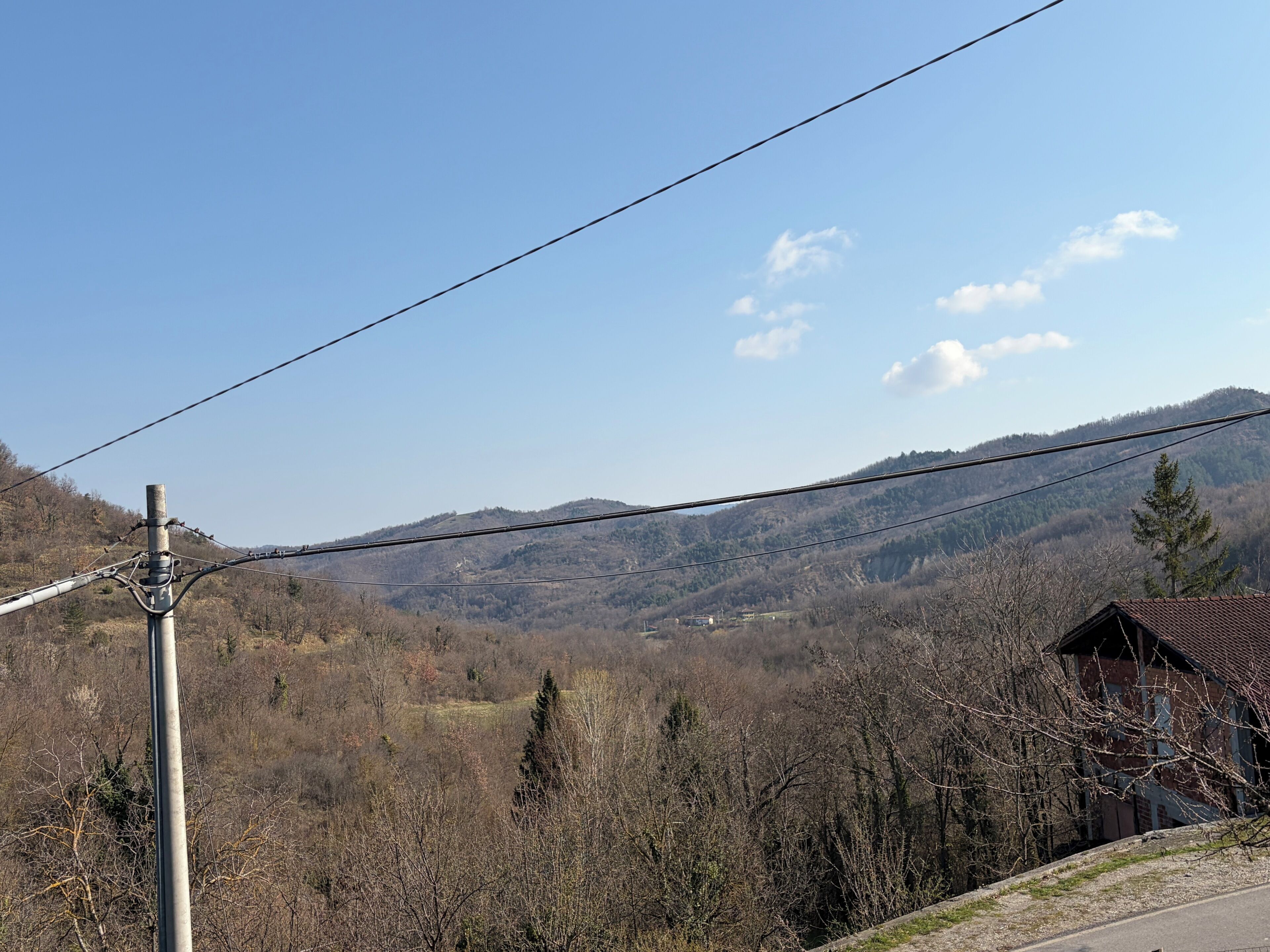 Paisaje rural con una casa, líneas eléctricas y un fondo montañoso.