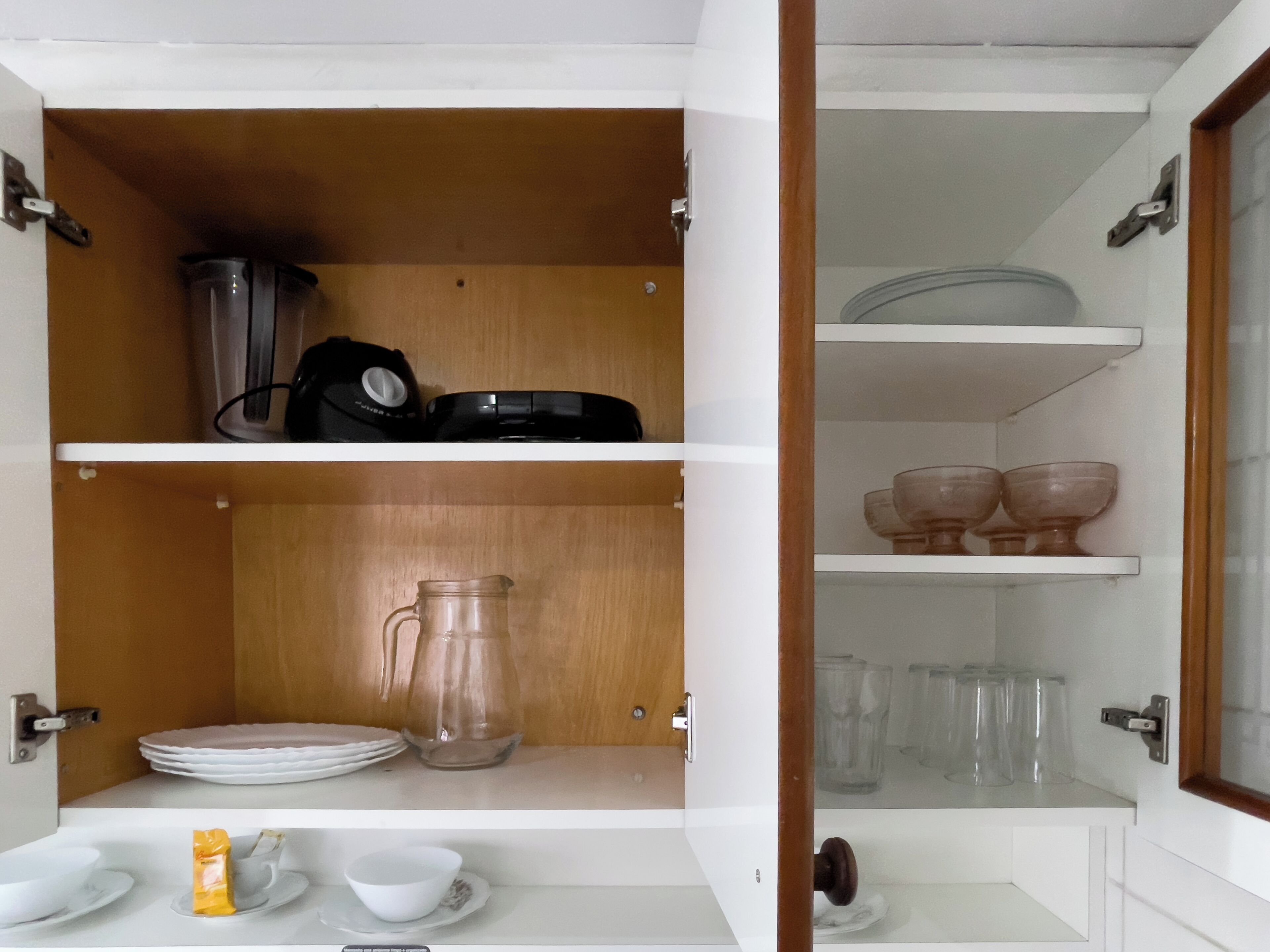 A kitchen with white cabinets, a coffee maker, a pitcher, and glassware.
