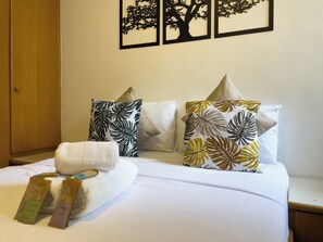 A neatly made bed with white linens, two pillows with tropical leaf patterns, and two towels with a tree design. - New York Plaza (São Paulo)