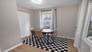 Ein Zimmer mit einem Esstisch, Stühlen, einem karierten Teppich, einem Fenster mit Vorhängen und einer Tür.