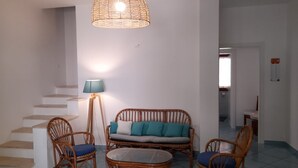 Un salón con sofá, dos sillones, una mesa, una lámpara y una escalera.