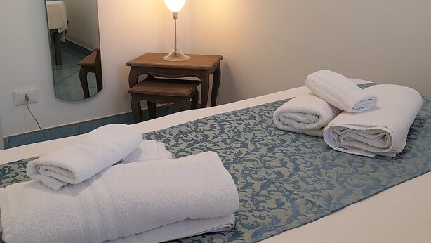 Habitación de hotel con cama, mesita de noche con lámpara, una silla y un espejo.