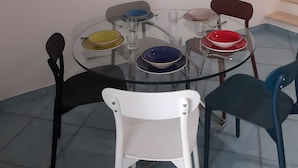 Un comedor con una mesa redonda de vidrio, seis sillas y un cuadro de un molino de viento en la pared.