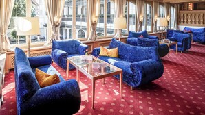 Ein Zimmer mit blau gepolsterten Sofas, einem Glastisch und einem roten Teppich mit Muster.