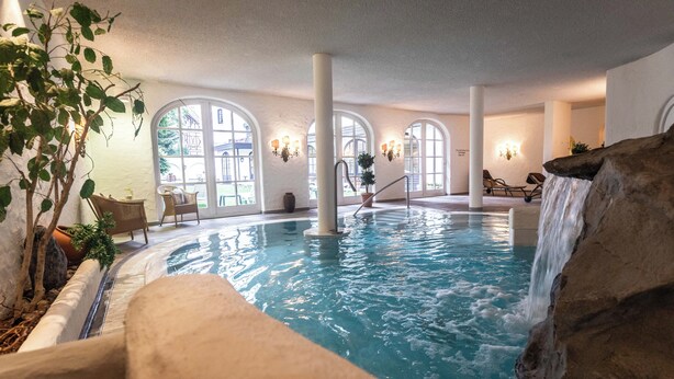 Ein Innenpool mit Wasserfall, großen Bogenfenstern und Sitzbereichen im Innenbereich.