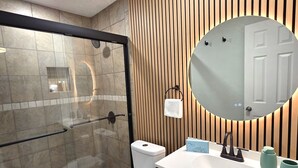 Moderni kylpyhuone, jossa on lasiseinällä varustettu suihku, wc, peilillä varustettu pesuallas ja seinässä puupanelointi.