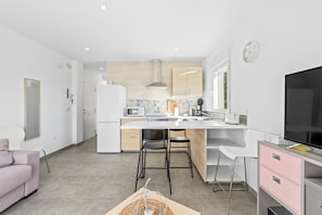 Una cocina moderna con una isla central, armarios blancos y un televisor de pantalla plana.