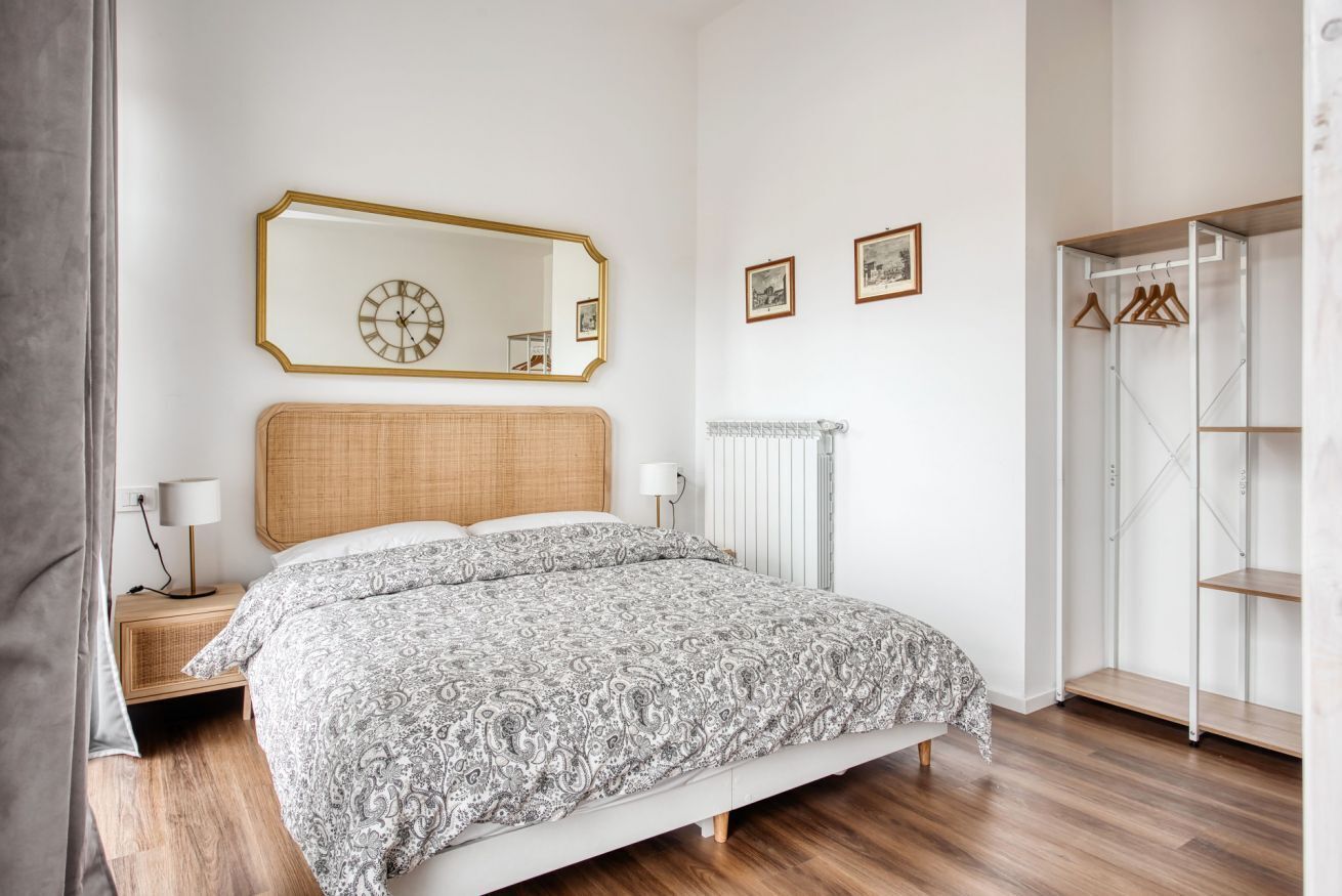 A bedroom with a bed, a bedside table, a mirror, a radiator, and a wardrobe.