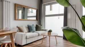 Una sala de estar moderna con un sofá, una mesa de centro redonda, una mesa de comedor con sillas, un espejo grande y una ventana con cortinas.