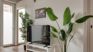 Una sala de estar con un televisor de pantalla plana sobre un soporte blanco, una planta grande en maceta y un mapa del mundo en la pared.