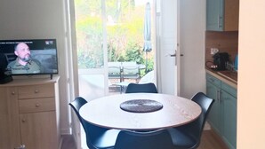A dining area with a round table, chairs, a ceiling fan, and a television on a cabinet.