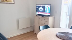 A room with a round table, a television on a cabinet, a radiator, and a framed picture on the wall.