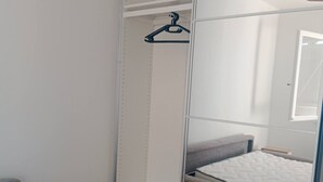 A bedroom with a bed, a grey sofa, a wardrobe with a mirror, and a hanging rack.