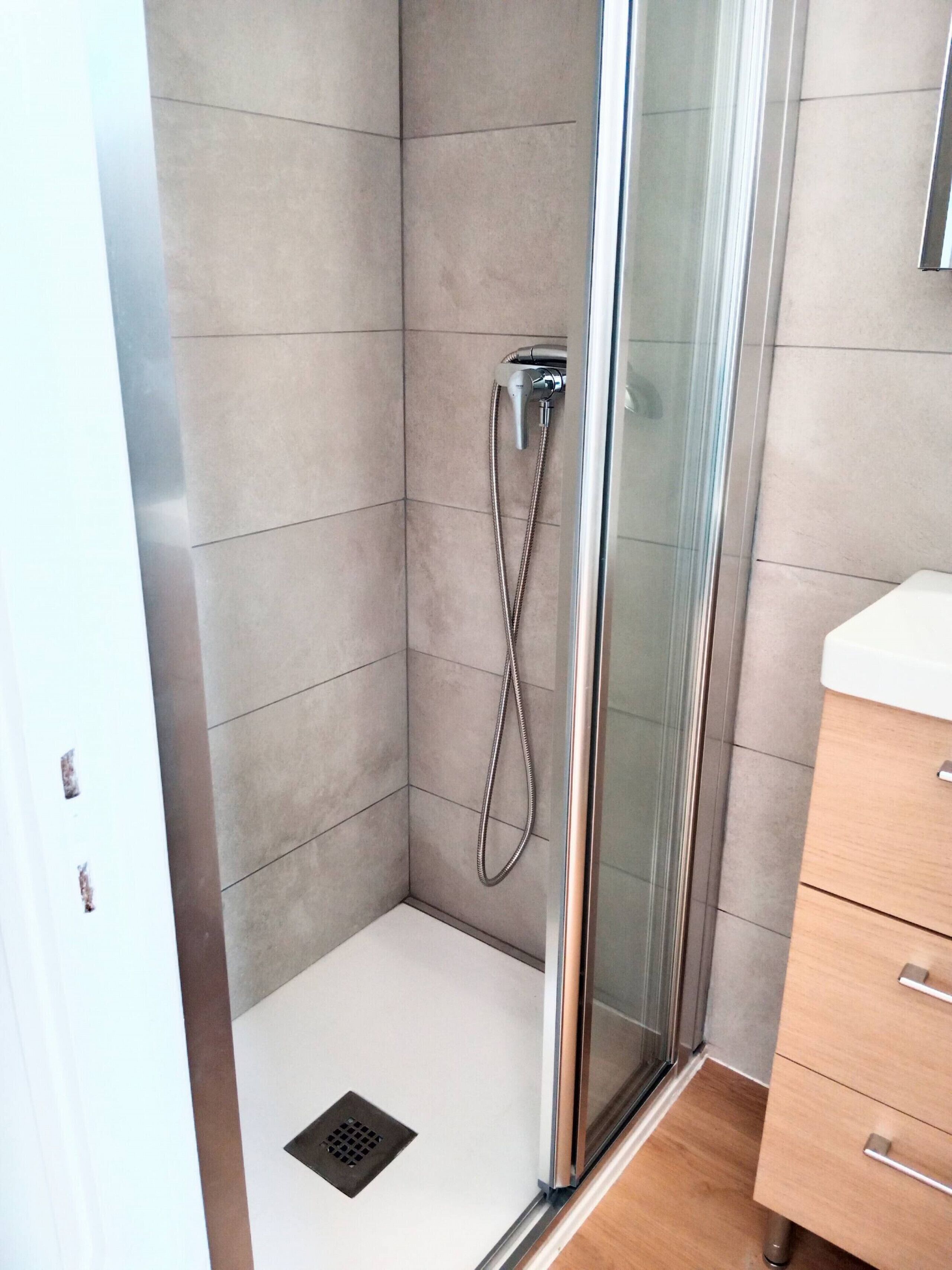 A modern shower with a glass door, a white sink, and a wooden cabinet in a bathroom.