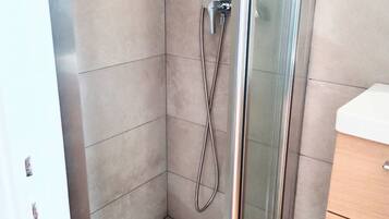 A modern shower with a glass door, a white sink, and a wooden cabinet in a bathroom.