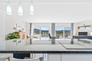 Une cuisine moderne dotée d’un grand îlot central, d’un coin repas avec des chaises, d’un canapé et d’une vue sur les montagnes grâce à de grandes fenêtres.