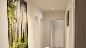 Un pasillo con suelo de madera, un cuadro con temática de bosque y una puerta al final.