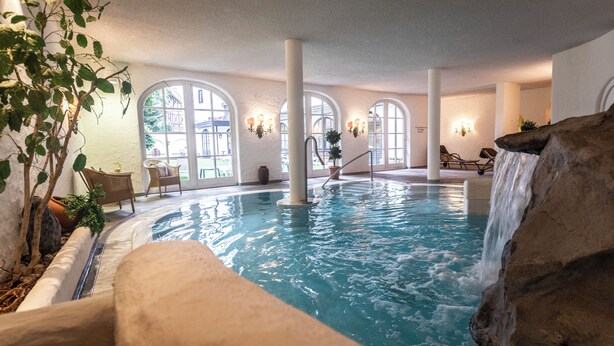 Piscina interior con cascada, ventanas amplias y zonas de estar.