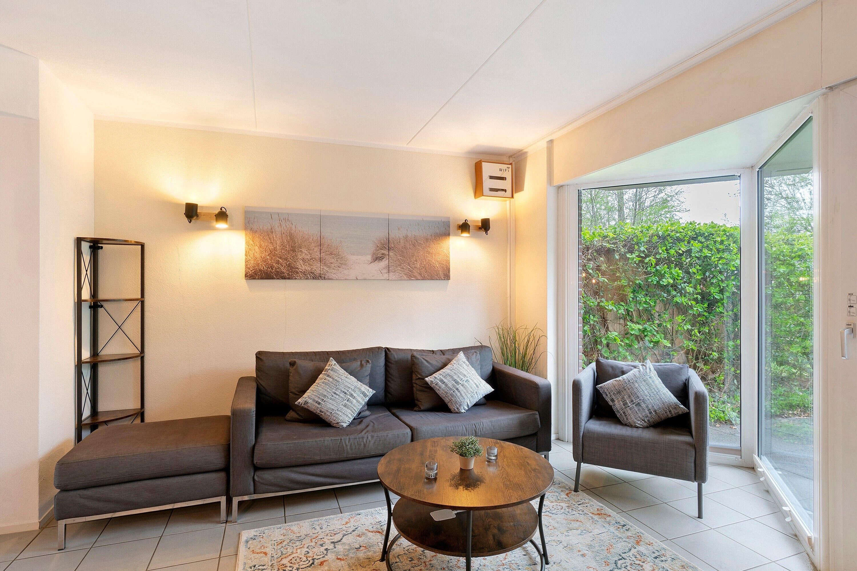 A modern living room with a sofa, armchair, and coffee table, a bookshelf, and a painting on the wall.