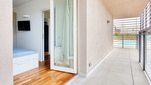 Ein modernes Hotelzimmer mit Holzboden, einem Bett und einer Schiebetür zu einem Balkon mit Blick auf einen Pool.