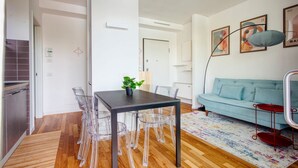 Ein modernes Wohnzimmer mit Esstisch, klaren Stühlen, einem hellblauen Sofa und einem farbenfrohen Teppich.