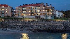 Ein mehrstöckiges Hotel mit Balkonen, einer Steinsichtmauer und Blick auf den Strand.