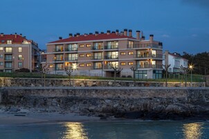 Un hotel de varios pisos con balcones, un muro de piedra y vista al mar.