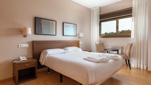 Ein Hotelzimmer mit einem großen Bett, Nachttischen, einem Sessel, einem kleinen Tisch und einem Fenster mit Vorhängen.