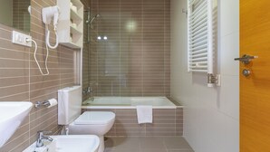 Ein Badezimmer mit Badewanne, Toilette, Bidet und einem an der Wand befestigten Föhn.