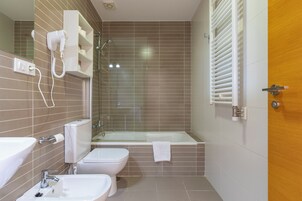 Un baño con bañera, inodoro, bidé y un secador de pelo fijado en la pared.