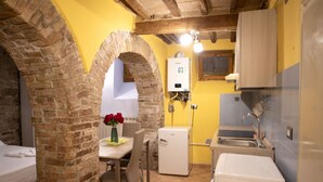 A compact kitchen with a refrigerator, sink, and a dining area with a table and chairs. - Cozy suite in the heart of Perugia, perfect for 2 guests.Elegant room, comfortable living room and kitchen equipped to feel right at home.The unique detail? The natural stone walls, which give charm and character to the environment.Bright and well-kept,  (Perugia)