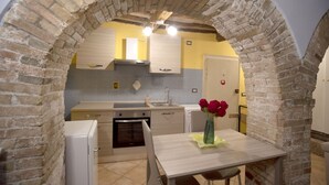 A kitchen with a brick archway, a sink, a stove, and a table with a vase of flowers. - Cozy suite in the heart of Perugia, perfect for 2 guests.Elegant room, comfortable living room and kitchen equipped to feel right at home.The unique detail? The natural stone walls, which give charm and character to the environment.Bright and well-kept,  (Perugia)
