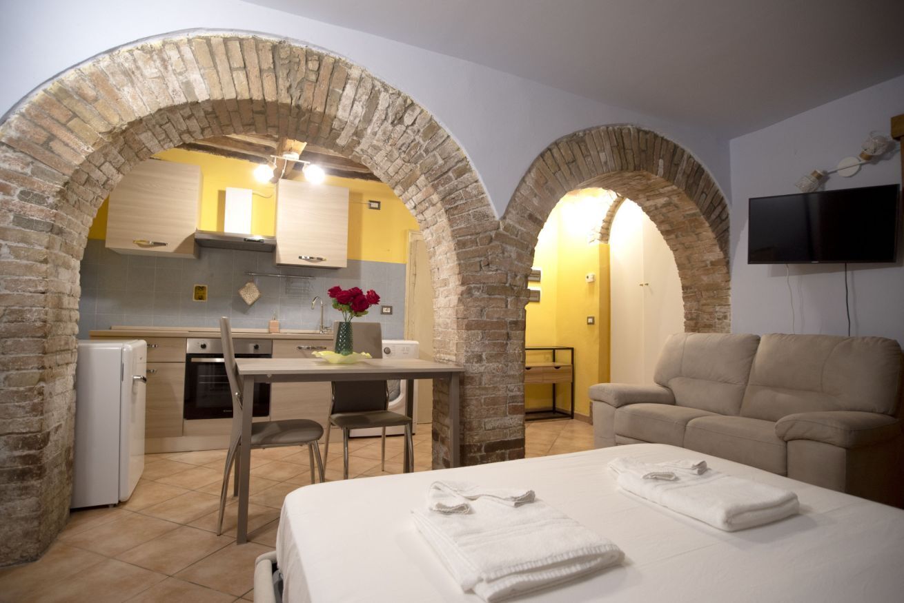 Une pièce comprenant un lit, un canapé, un téléviseur et un coin cuisine, le tout visible à travers une arche.