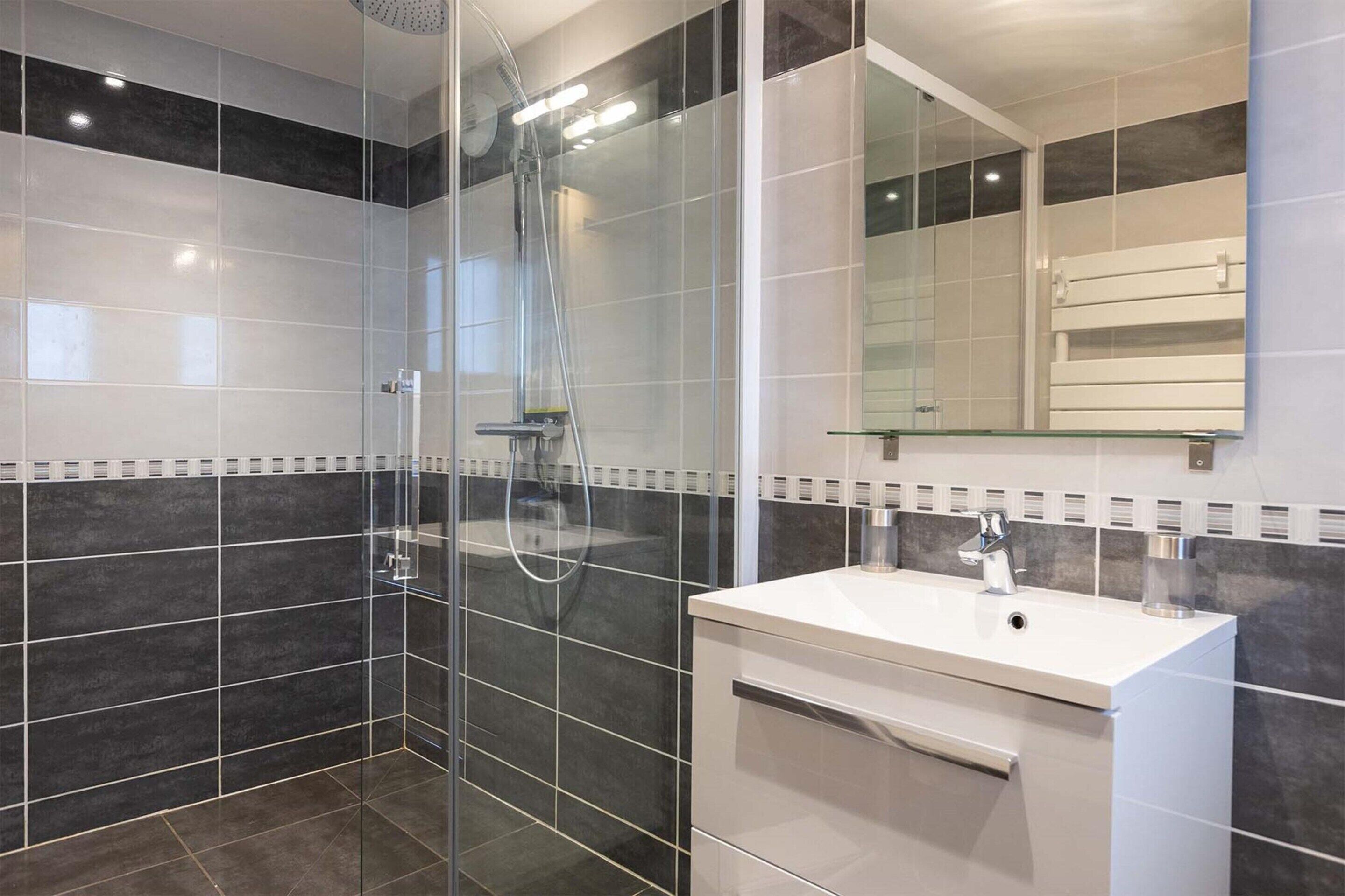 Un baño moderno con ducha de vidrio, lavamanos blanco y espejo sobre el lavamanos.